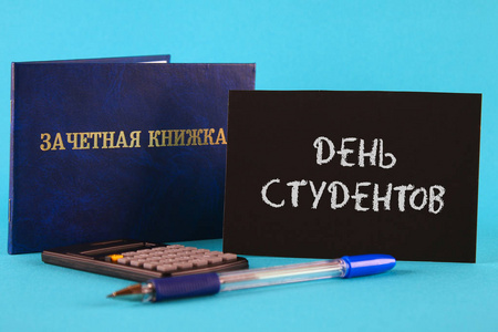 一本带有俄语铭文的蓝色书学生的记录册。钢笔, 计算器在蓝色背景。俄语学生日题词