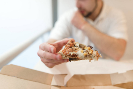 一个男人手里拿着一块披萨。这个男人吃披萨。专注于一块披萨