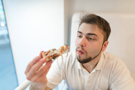 有胡子的男人在嚼披萨学生吃美味的比萨饼和看着他用心