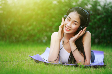 妇女听音乐与耳机和铺设在草地上
