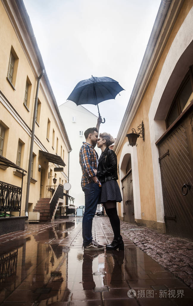 在雨天一对幸福的情侣站在一把雨伞下的城市街道