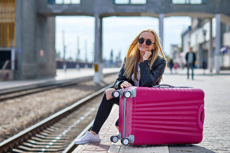 一个女孩，一个粉红色的手提箱站在火车站