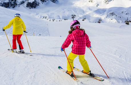妇女滑雪与女儿在雪在一个晴朗的天在群山