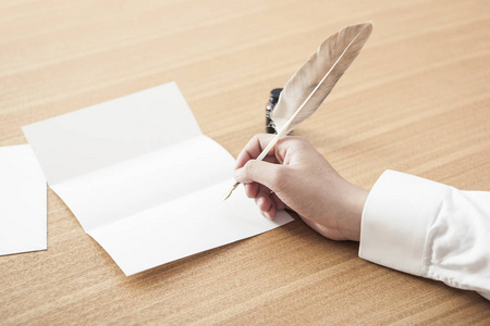 男子在日光木桌上把羽毛笔浸入墨水罐写一封信