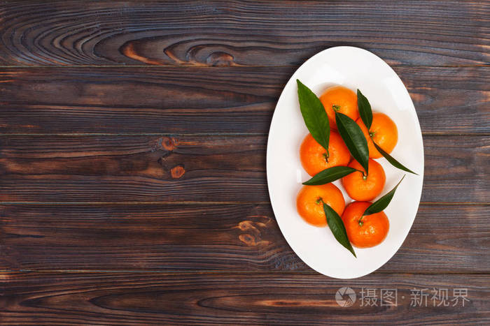 成熟的普通话与叶子, 橘橙在木桌背景与拷贝空间。柑橘类水果在盘子里。顶部视图