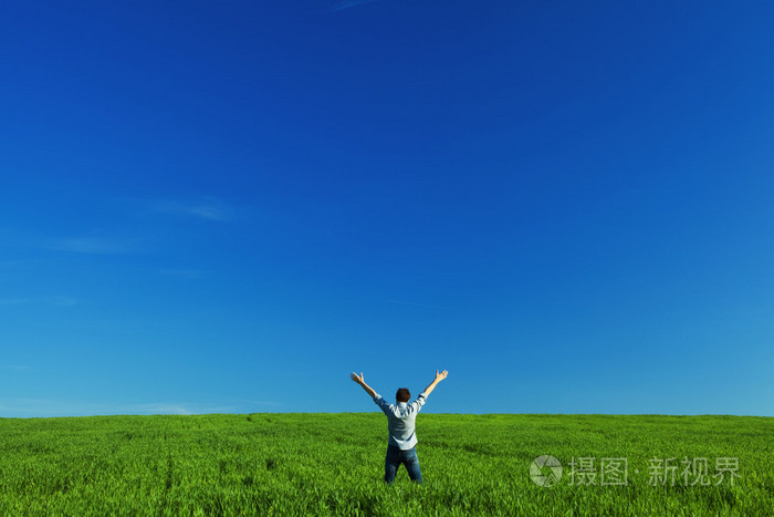 年轻人张开双臂在绿色的田野上迎着蓝天
