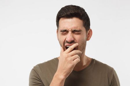 无聊的年轻人打呵欠沉睡的年轻人打呵欠, 醒来, 用手闭上嘴巴, 在灰色