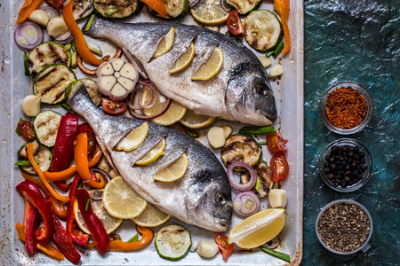 多拉达鱼与蔬菜, 柠檬, 香料和绿色的蓝色背景