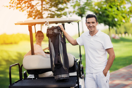 一个女人坐在高尔夫球车的轮子后面, 一个在前台, 拿着一包高尔夫球杆