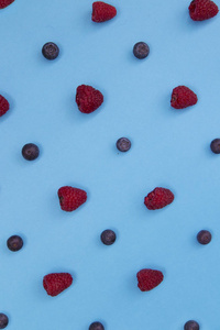 蓝色背景下新鲜蓝莓和覆盆子的彩色水果图案
