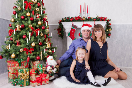 圣诞节或新年庆祝。幸福的年轻家庭在圣诞树与壁炉