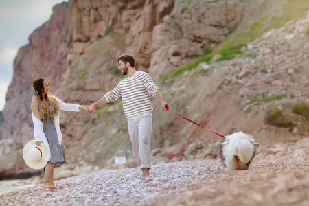 时尚快乐情侣牵手在沙滩上与毛茸茸的狗散步照片