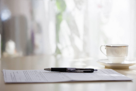 白色咖啡杯特写与文件和钢笔站在桌子上, 模糊的背景