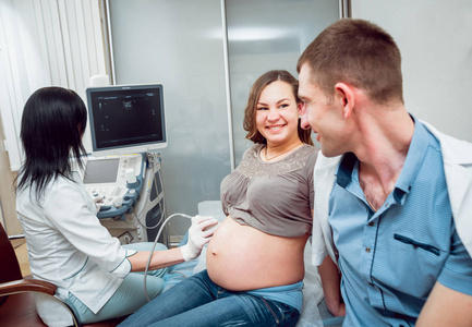 女医生和年轻孕妇与丈夫的病人。超声波设备。诊断.超声