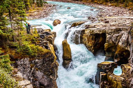 两个人看着 Sunwapta 瀑布在加拿大落基山脉的碧玉国家公园