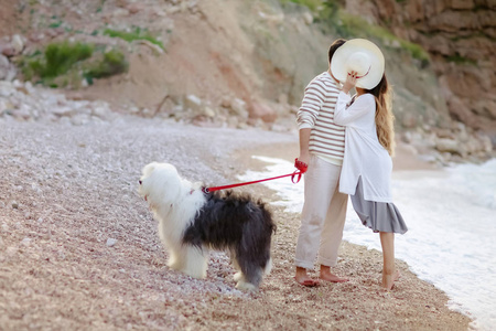 满长的年轻夫妇站在海滩上毛茸茸的狗和亲吻隐藏在帽子后面