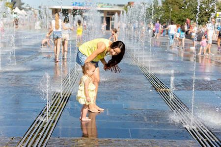 母亲和孩子在炎热的夏天一天玩水射流的喷泉