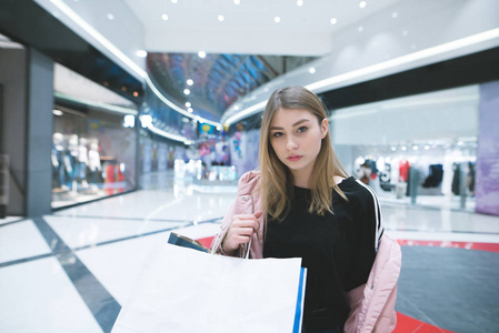 一个时尚的女孩对购物中心背景的肖像。那个女孩在购物中心购物。看镜头
