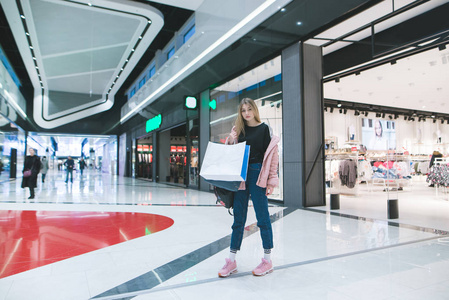 一个时尚的女孩在她的手购物袋站在商场和服装店。购物理念