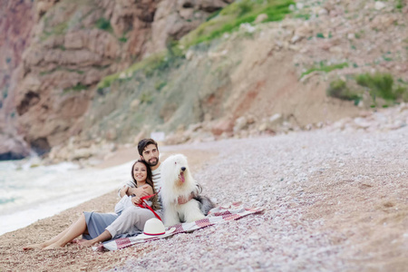 年轻幸福的夫妇休息与狗坐在海滩