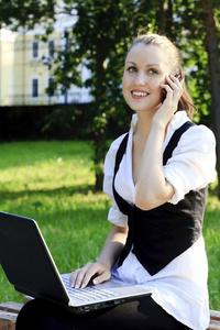 年轻漂亮的女人坐在公园长凳上的便携式计算机