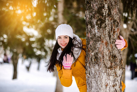 美丽的女孩在雪躲在一棵树后面的肖像