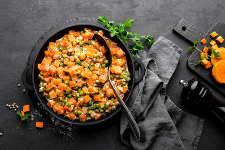 胡萝卜炖鲜青豆在 stewpan, 蔬菜炒黑背景, 顶部视图