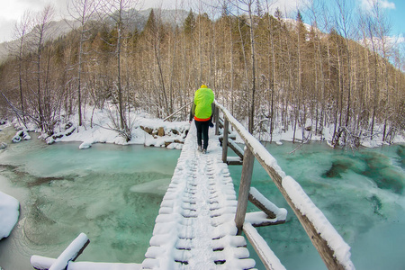 在山上冬天森林里的一个冰冻的绿松石冰河上的桥上行走的女孩