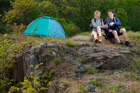 两个徒步旅行者在森林的帐篷附近休息着喝着热茶。旅行, 假期, 假期和冒险概念。山风景背景