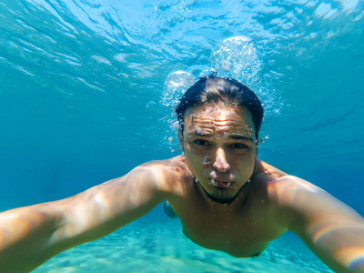 年轻的男性潜水员在海里游泳, 在蓝色的水, 使一个自拍照片