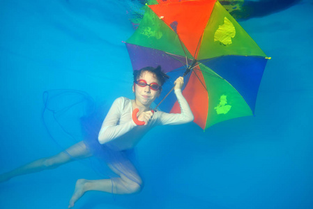 小女孩在水池里游泳, 带着彩色雨伞在水里游泳。肖像.水平视图