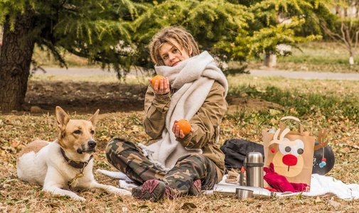 年轻欧洲妇女与非洲人发型在公园在秋天与她的狗演奏与果子