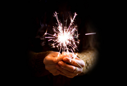 在晚上的烟火女孩的手拿着一个烟火.在黑暗中.晚上.隔离在照片