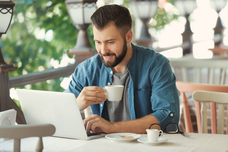 年轻的博客写手在户外咖啡馆喝咖啡和使用笔记本电脑