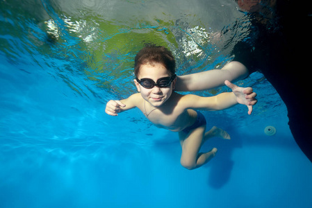 体育小男孩游泳与一个教练在水下在池中的蓝色背景, 看着相机和微笑。肖像。在水下射击。横向方向