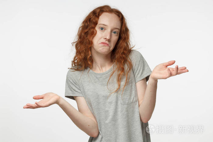 我不知道红头发的女孩孤立在灰色的背景是在亏损显示无助的手势与手臂