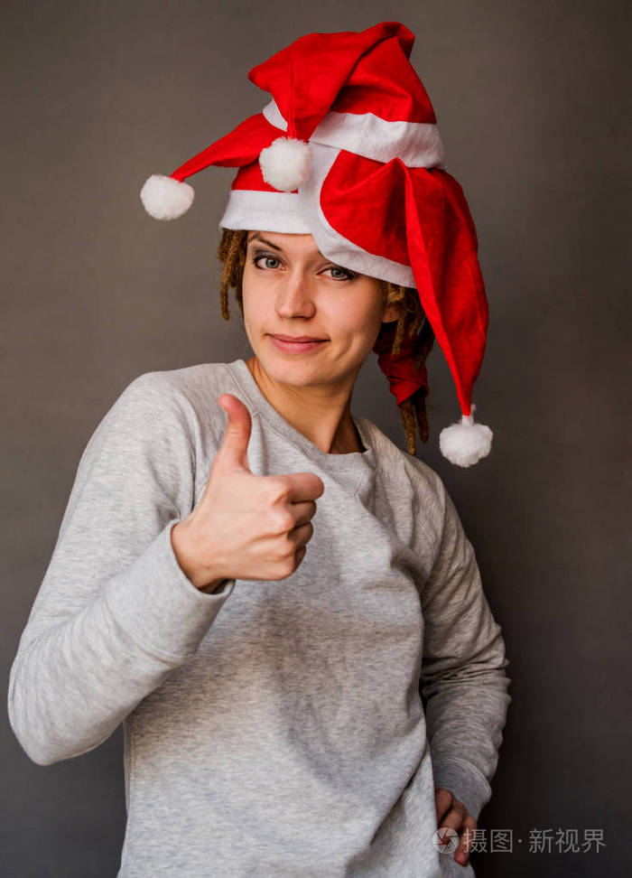 快乐自信的女人在圣诞老人的帽子拿着拇指