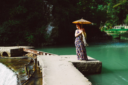 redhaired 女士穿着一件长裙穿过亚洲公园, 手持一把中国雨伞