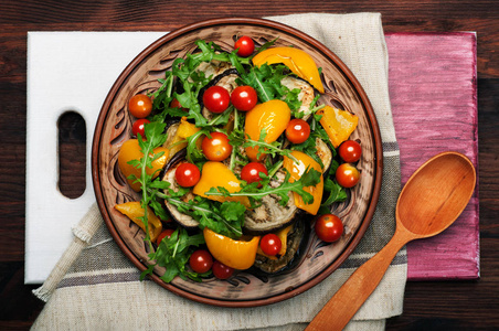 地中海美食。温暖的沙拉菜烤的辣椒 茄子 芝麻菜叶子和樱桃番茄的褐色粘土板上。素食主义者的概念。膳食低热量食品