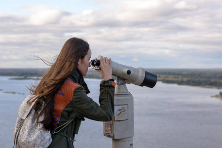 一个年轻的女游客在观察甲板上寻找通过望远镜在下诺夫哥罗德城市全景
