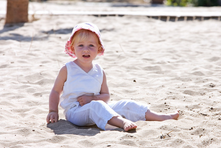 小孩坐在沙滩上戴着粉红色的帽子