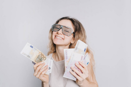 拿走我的钱年轻快乐的白种女孩与眼镜和白色的 t-shirt 持有欧元钞票