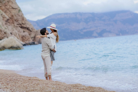 愉快的人拥抱举起他的美丽的妇女站立在海滩与峭壁在背景, 全长