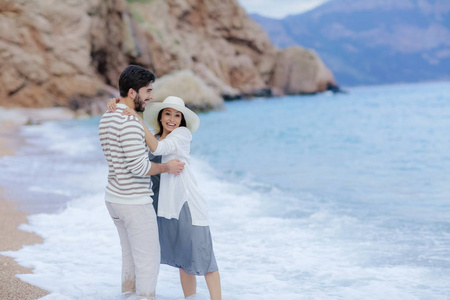 愉快的人拥抱他的美丽的妇女站立在海滩与峭壁在背景