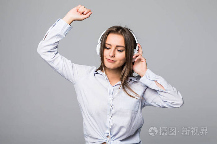 快乐的女人在衬衫上听音乐, 在地板上用紧闭的眼睛跳舞。孤立的灰色背景