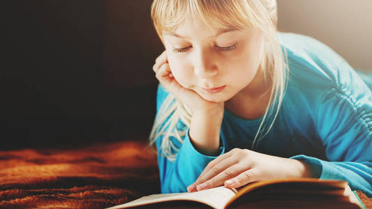 一个穿着蓝色上衣的金发女郎躺在黑暗的房间里, 读着一本绿色的书