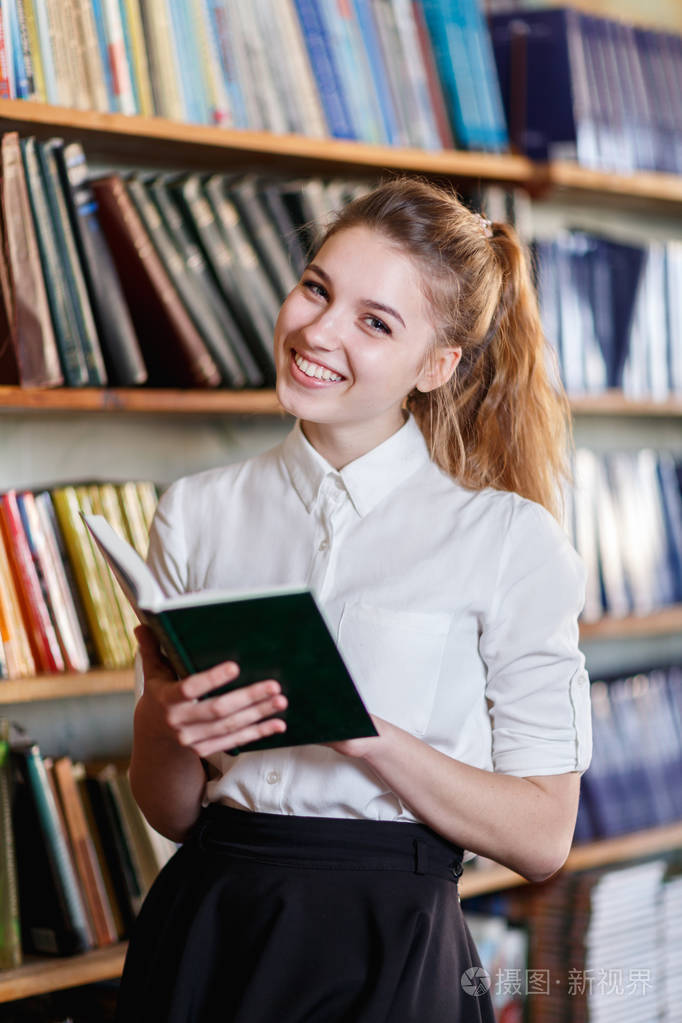 一个年轻的女孩,拿着一本书在图书馆里的肖像