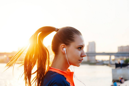 年轻运动的女孩慢跑，在河边，晚上听音乐头戴式耳机