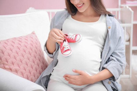 怀孕的女人在家里抱着婴儿鞋