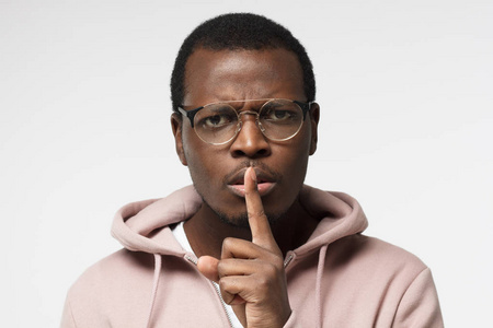 近距离拍摄英俊的黑人男性与嘘手势, 要求沉默或安静, 孤立的灰色背景